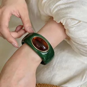Close-up of a marbled green acrylic bangle with a large amber resin stone on a model's wrist