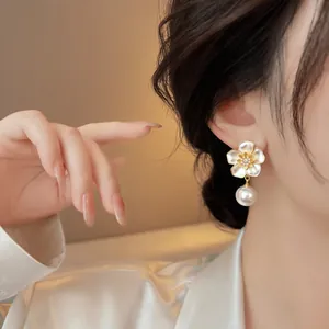Elegant vintage style white enamel flower and pearl drop earring worn by a model.