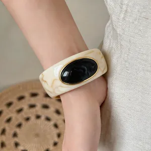 Macro view of a chunky marbled acrylic bangle with a black oval resin stone.