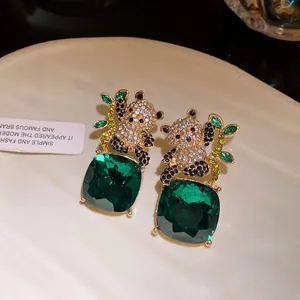 Detailed macro view of crystal panda earrings with emerald green square faceted gemstones