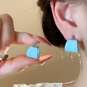 Gros plan de boucles d'oreilles sac en émail bleu clair en forme de U sur l'oreille et la main
