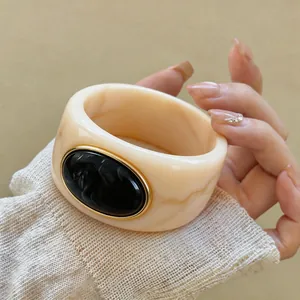 Detail view of a chunky marble-patterned acrylic bangle with a black oval centerpiece.