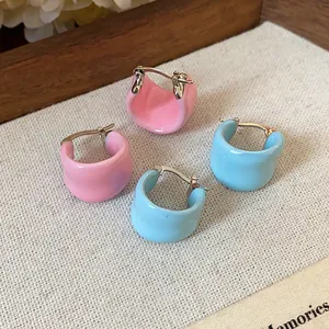 Détail en gros plan de boucles d'oreilles créoles en émail rose et bleu sur fond texturé