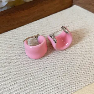 Gros plan sur la finition émail rose des boucles d'oreilles en U sur tissu de lin