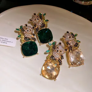 Close-up of sparkling rhinestone panda earrings with green and champagne square pendants.