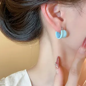 Gros plan détaillé d'une boucle d'oreille en émail bleu clair en forme de U sur une oreille