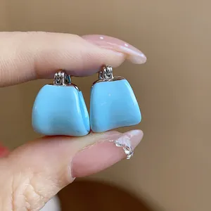 Gros plan de boucles d'oreilles créoles en émail bleu clair en forme de U tenues entre les doigts