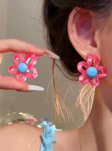 Detailed view of pink resin flower stud earrings with a blue center on a model's ear