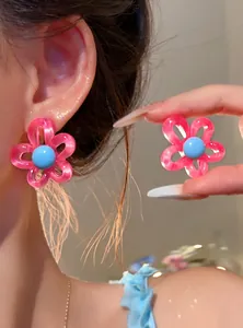 Detailed view of sweet pink resin flower earrings with blue centers worn on model's ear