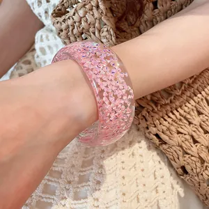 Detailed shot of pink glitter resin bangle on wrist with summer straw bag background