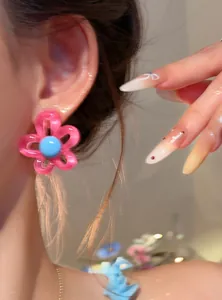 Detailed shot of pink resin flower earring with blue center on model's ear