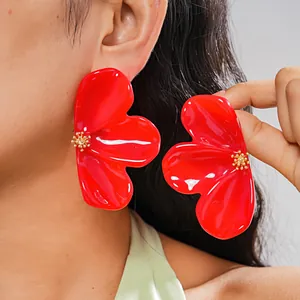 Close-up detail of large red resin flower earrings with glossy finish for resort style