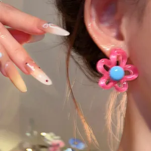 Close-up detail of a sweet pink resin flower earring with a blue center on a model's ear