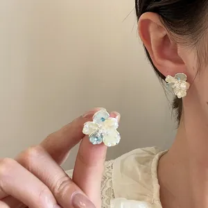 Detailed close-up of elegant crystal and pearl flower stud earrings worn on female ear