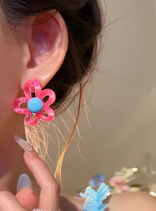 Close-up of a stylish pink resin flower stud earring with a light blue center on a person's ear