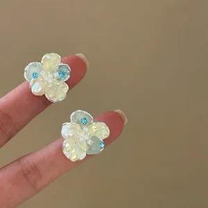 Detailed close-up showing translucent crystal and pearl flower stud earrings on fingers