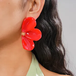 Detailed view of vibrant red resin flower earring with golden stamen detail on a model.