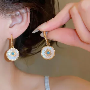 Macro detail of gold-plated sunburst earrings with mother of pearl and turquoise center