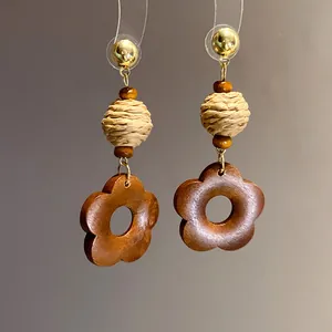Detailed view of handmade ethnic style earrings featuring raffia balls and wooden flower pendants