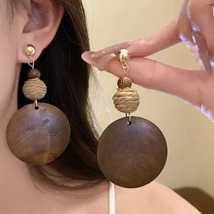 Detailed view of handmade raffia and round wooden dangle earrings on a model's ear