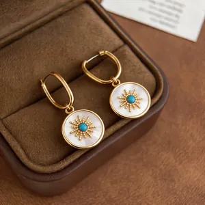 Close-up of gold plated sunburst earrings with mother-of-pearl and turquoise center