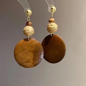 Detail of ethnic retro wooden circular pendant earrings with woven raffia ball texture