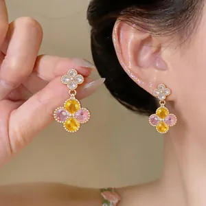 Nahaufnahme von bunten Blumen-Zirkon-Ohrringen am Ohr und in der Hand gehalten.