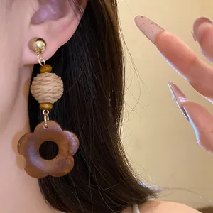 Detailed view of bohemian style raffia and wooden flower drop earrings worn on model's ear