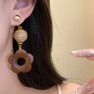 Close-up shot of retro ethnic raffia and wooden flower pendant earrings worn on a person's ear
