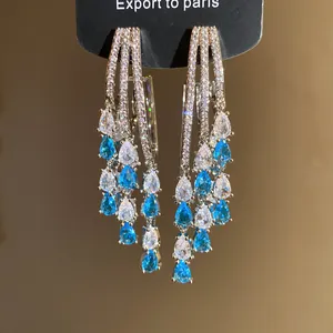 Close-up of elegant 18k gold plated teardrop tassel earrings with blue and clear zircons.