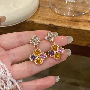 Detailaufnahme von goldenen Blumenohrringen mit bunten Zirkonsteinen in der Hand