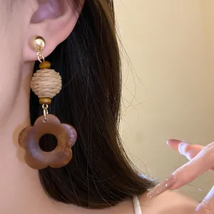 Close-up of vintage raffia and wood flower drop earrings worn by a model