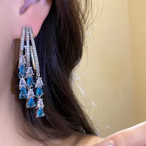 Close-up of blue and white cubic zirconia waterdrop tassel earrings worn on ear.