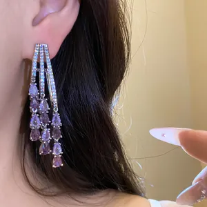 Close-up view of elegant sparkling tassel earrings with purple pear-shaped zircons on ear