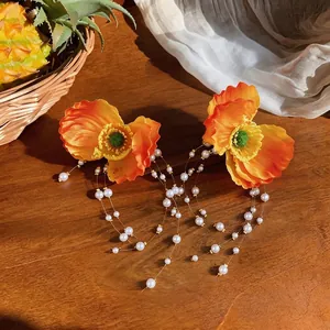 Elegant orange fabric flower earrings with long pearl tassels on rustic wooden table background