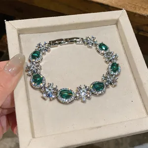 Detail view of a silver flower bracelet with oval green zircons in a beige jewelry box.
