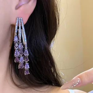 Macro detail view of elegant purple zircon water drop tassel earrings worn on a female ear.