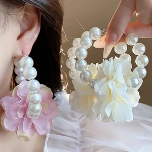 Primo piano di eleganti orecchini a cerchio con grandi perle e fiore di stoffa rosa