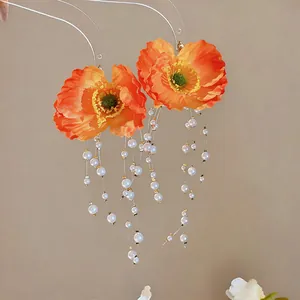 Detail view of orange fabric poppy earrings with elegant long pearl tassels and gold accents