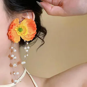 Macro detail of vibrant orange fabric flower earrings with elegant pearl tassels