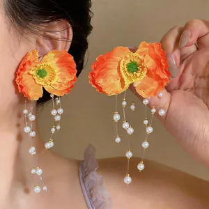 Close-up of vibrant orange fabric flower earrings with pearl tassels on an Asian model