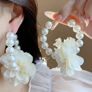 Primo piano di eleganti orecchini a cerchio con fiori di stoffa e perle su una modella.