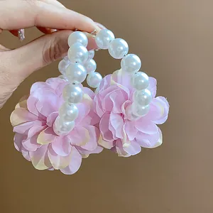 Dettaglio di orecchini a cerchio con fiori in tessuto rosa e perle bianche eleganti.