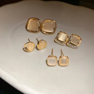 Close-up detail of elegant gold stud earrings set with shimmering cat's eye stones and crystals.
