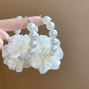 Dettaglio di orecchini a cerchio con perle bianche e grandi fiori in tessuto