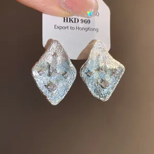 Detailed view of silver diamond-shaped earrings with wrinkled texture and zircons.