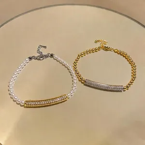 Two elegant gold-plated and pearl zircon curved bar bracelets displayed on a golden mirror tray