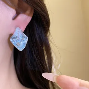 Detailed macro view of silver pleated diamond stud earrings with zircon accents on ear