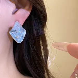 Detail shot of elegant silver wrinkled rhombus stud earrings with embedded zircon on ear