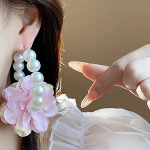 Dettaglio ravvicinato di orecchini a cerchio con perle e fiore in tessuto rosa chic